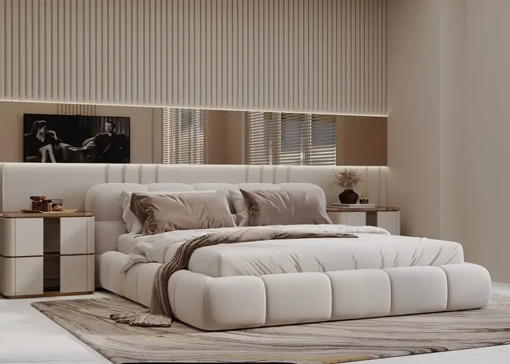 A low-profile Upholstered Bed featuring a thick, segmented padded frame and a wide integrated headboard in cream fabric.